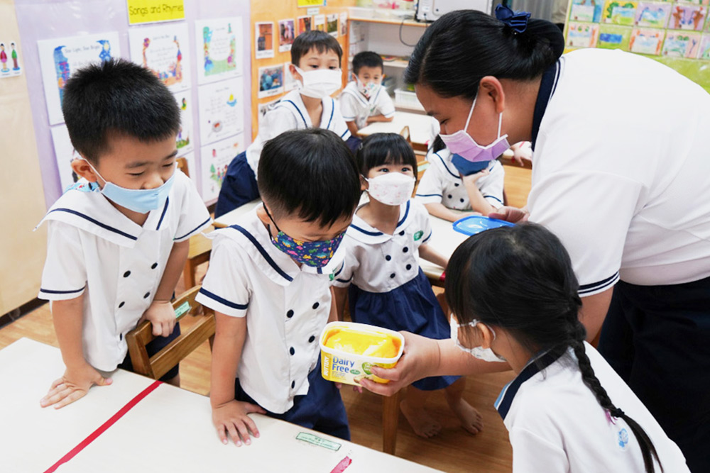 Most of the ingredients are new to the children. The teacher walks to each table to show the children the shape of the half-melted butter. (Photo by Chan May Ching)